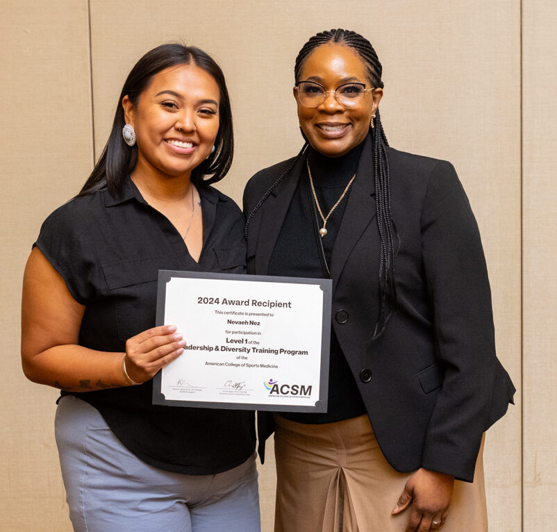 Two women smiling at the camera, one is holding a certificate