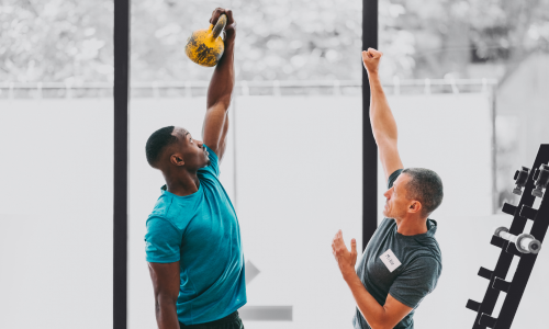 personal trainer coaching a man to do an overhead kettlebell lift